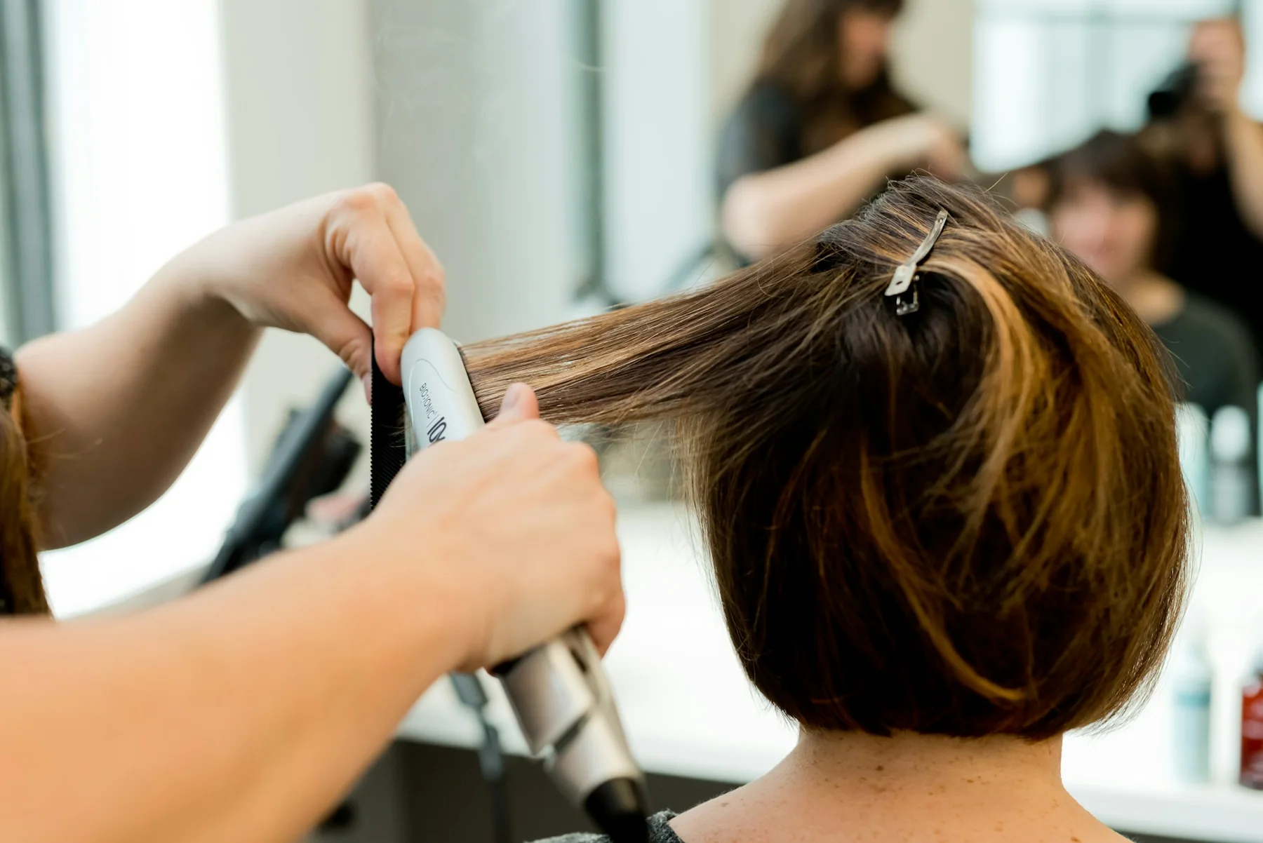 A stylist straightening a client’s hair with a flat iron in a salon